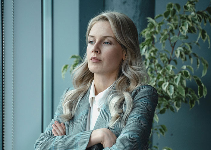 Young woman in a blazer with arms crossed, looking concerned, depicting micromanagement in a workplace setting.