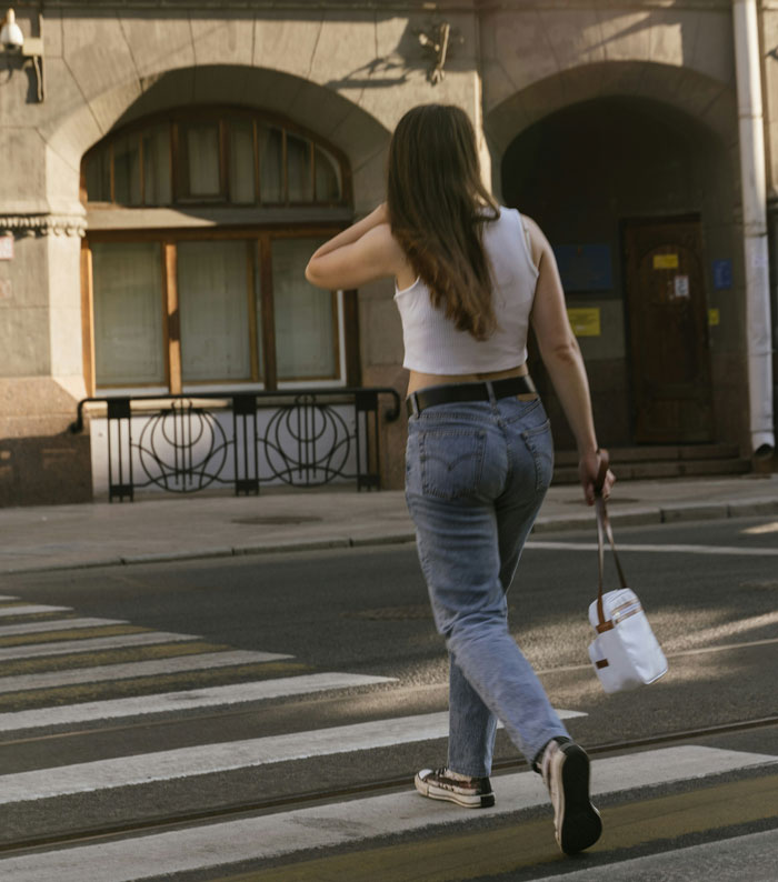 Woman walking on a city street crosswalk, representing women sharing inappropriate comments heard from men in public spaces.
