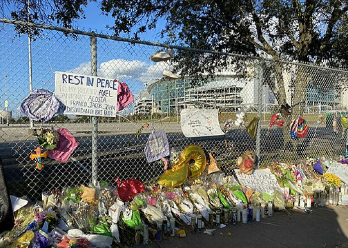 Memorial tribute with flowers, balloons, and notes attached to a chain-link fence under clear sky. - 27
