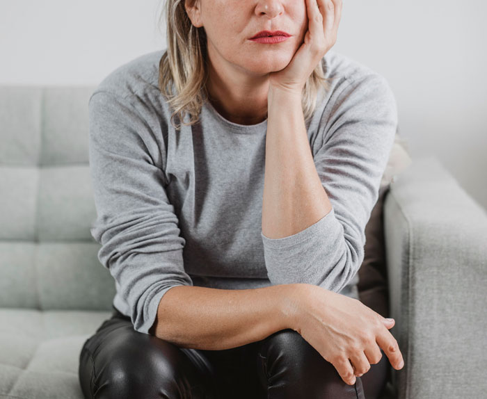 Woman sitting on couch looking thoughtful and pensive, reflecting during a moment of self-discovery and personal change.