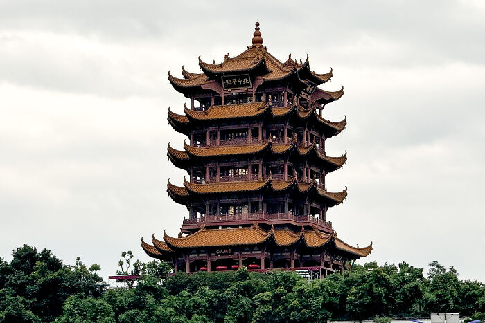 Ancient historic building with traditional Asian architectural design surrounded by greenery under a cloudy sky.