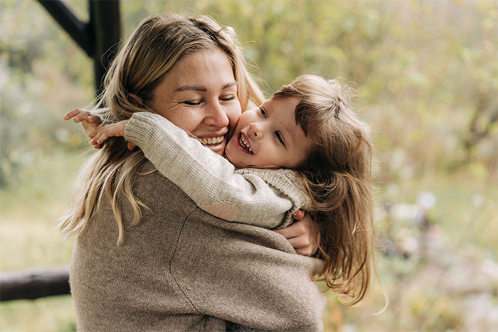 Woman hugging child outdoors, showing emotional connection but hesitating to share important news with dad.