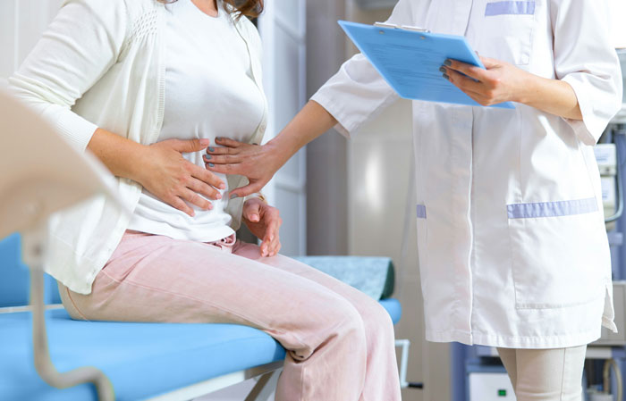 Paciente tocándose el abdomen mientras un médico revisa notas, ilustrando errores terribles en hospitales.