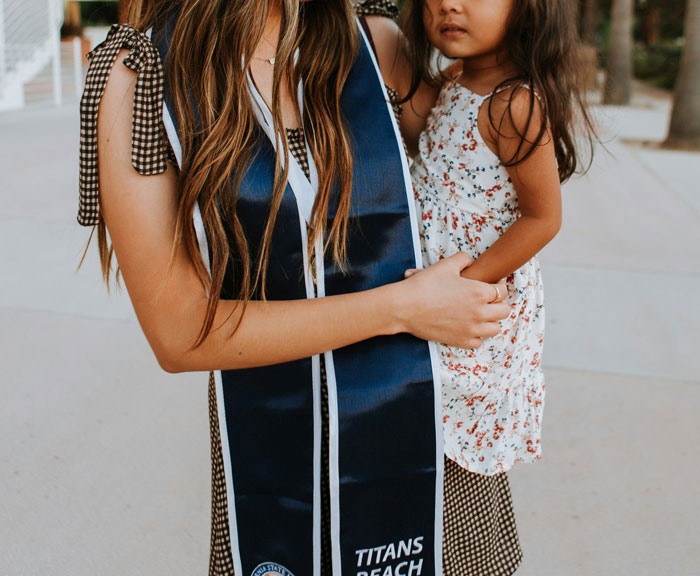 Woman in graduation attire holding a child outdoors, representing women sharing inappropriate comments heard from men in public spaces.