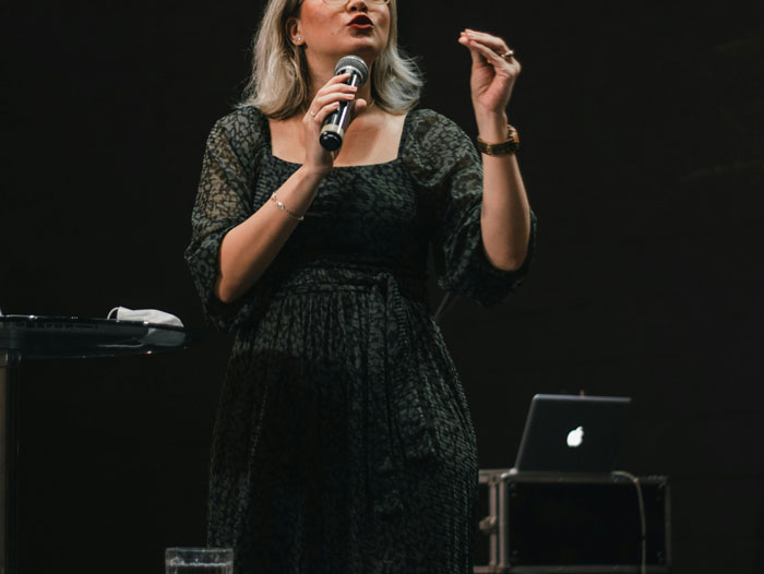 Woman speaking into microphone on stage during event, illustrating people regretting accepting a wedding invitation. - 5
