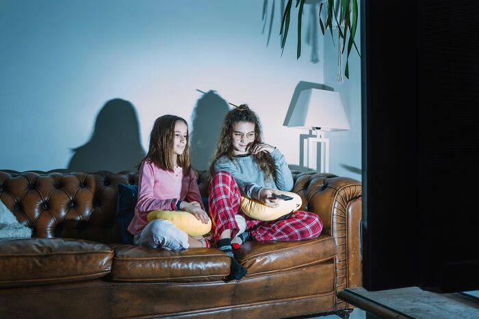 Two girls sitting on a couch watching TV at night, highlighting simple pleasures from the good old days and thank you notes era.