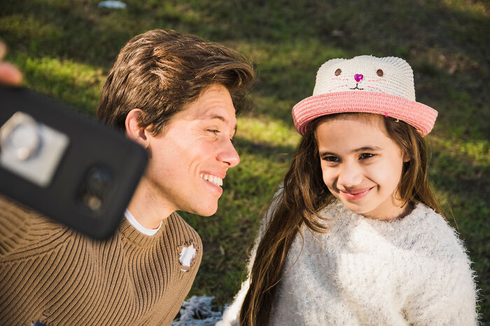 Young man and girl with a cute hat smiling outdoors while taking a selfie, illustrating normal people's habits viewed as creepy. - 26