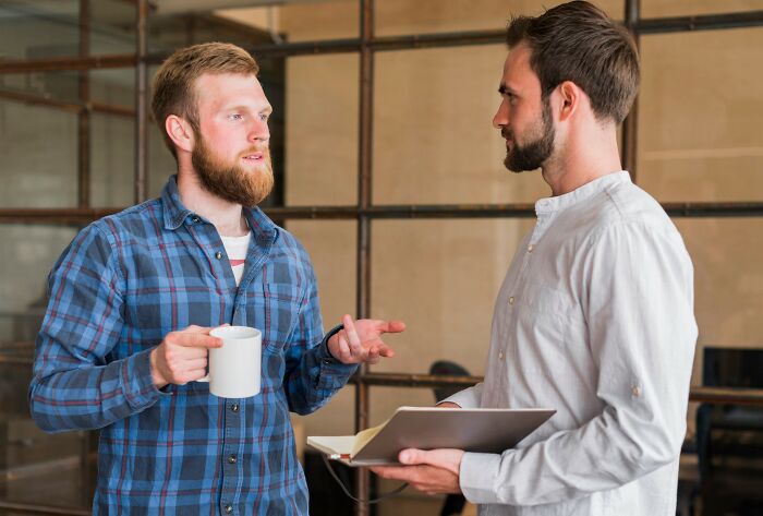 Two men discussing habits in a casual setting, one holding a coffee mug, illustrating normal people's habits found creepy online. - 15