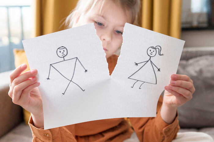Child holding torn paper with sad stick figure couple drawing illustrating signs a couple’s days are numbered