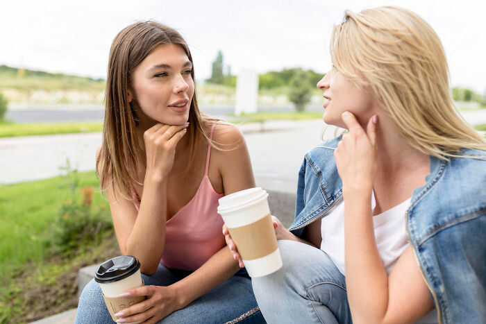 Two women drinking coffee outdoors, discussing signs netizens say reveal a couple’s days are numbered.