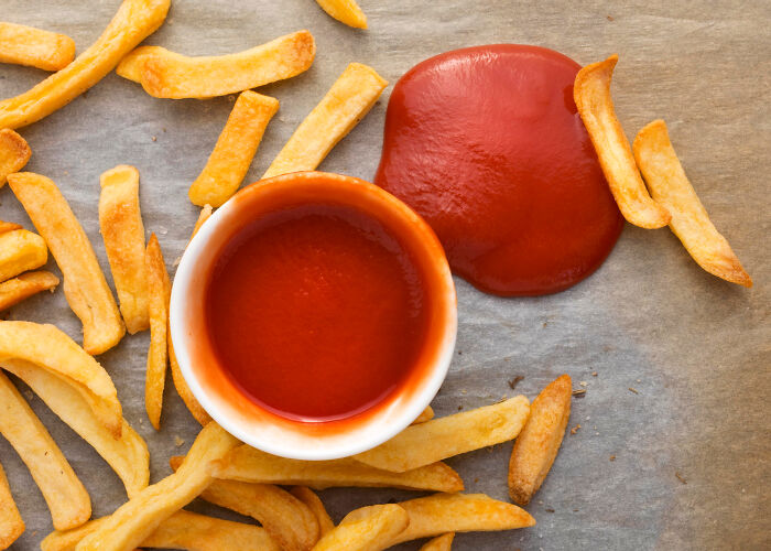 French fries scattered around a small bowl of ketchup with some ketchup spilled, illustrating unusual things people did in public.