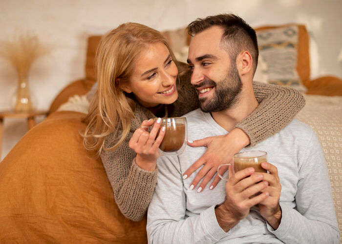 Couple sharing warm drinks on couch, smiling and embracing, illustrating signs that days are numbered in relationships.