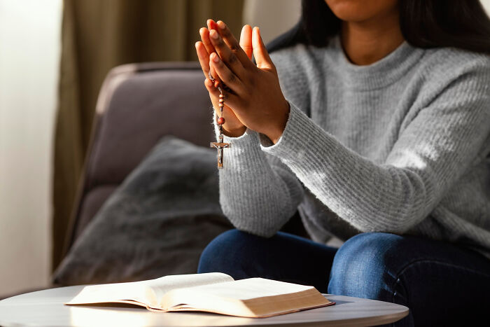 Person holding a rosary and praying over an open book, illustrating habits some netizens find really creepy. - 9