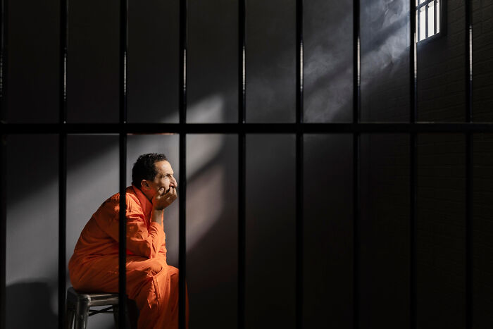 Man in orange prison jumpsuit sitting behind bars, representing creepy habits some netizens find unsettling. - 33