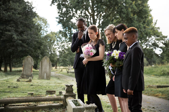 A diverse group gathered at a cemetery, mourning and holding flowers, reflecting on memories and thank you notes from the past.