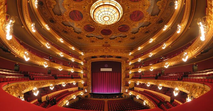 Interior of a beautifully restored historic building with ornate gold details and a large illuminated ceiling dome.