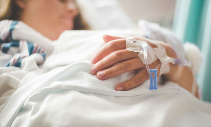Person lying in hospital bed with IV drip attached to hand, highlighting tips to stay safe and alive.