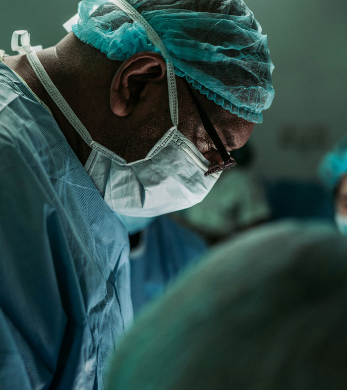 Médico en hospital usando mascarilla y gorro quirúrgico durante procedimiento en sala de operaciones.