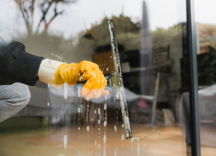 Person in yellow gloves cleaning a glass window, illustrating women sharing inappropriate comments heard from men in public spaces.