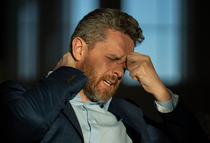 Man in a suit rubbing his eyes and neck, showing stress and frustration after wife leaves to find herself alone.