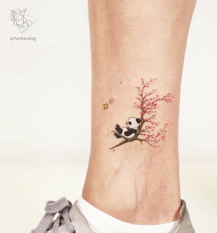 Small tattoo of a panda sitting on a cherry blossom branch with a shooting star on an ankle, popular tattoo design example.