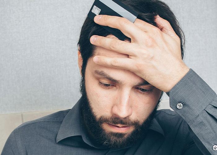 Man holding a credit card to his forehead looking stressed, illustrating one of the worst cheating stories.