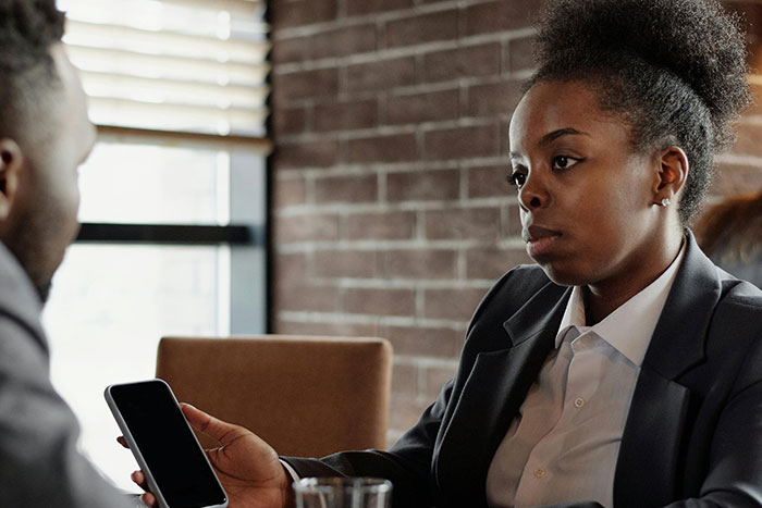 Woman in a business suit holding a phone during a serious conversation about microfeminisms with a male colleague.
