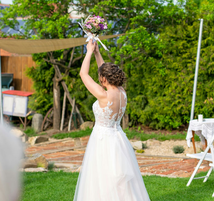 Bride in white wedding dress holding bouquet up in garden during outdoor ceremony for wedding invitation regret story - 18