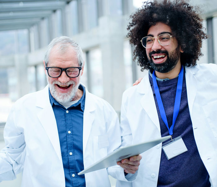 Two doctors in white coats laughing and discussing medical mistakes made in hospitals with a tablet device.