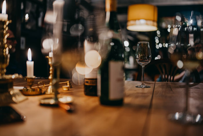 Wine glasses and bottles on a wooden table in a dimly lit room, illustrating women sharing inappropriate comments.