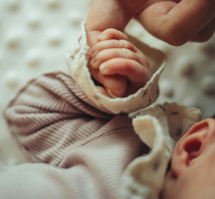 Newborn baby hand held gently, symbolizing husband feels sick after realizing who their son is named after. - 8