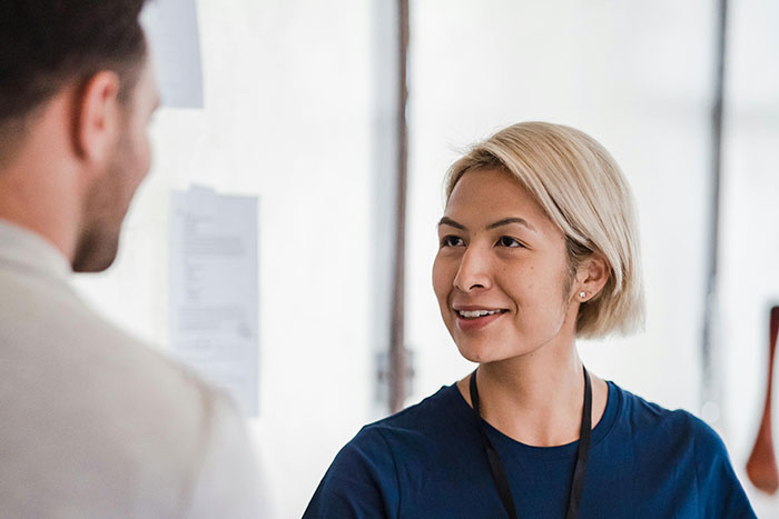 Woman with blonde hair smiling and talking to a man indoors, illustrating microfeminisms in casual conversation.