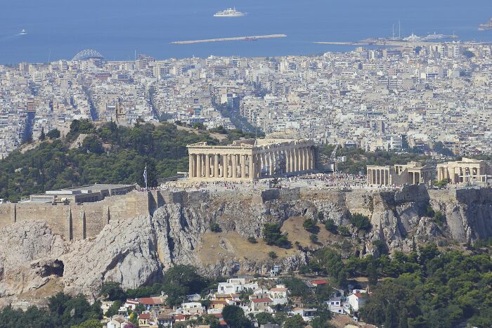 Aerial view of a historic cityscape with ancient ruins and dense urban buildings under clear skies.
