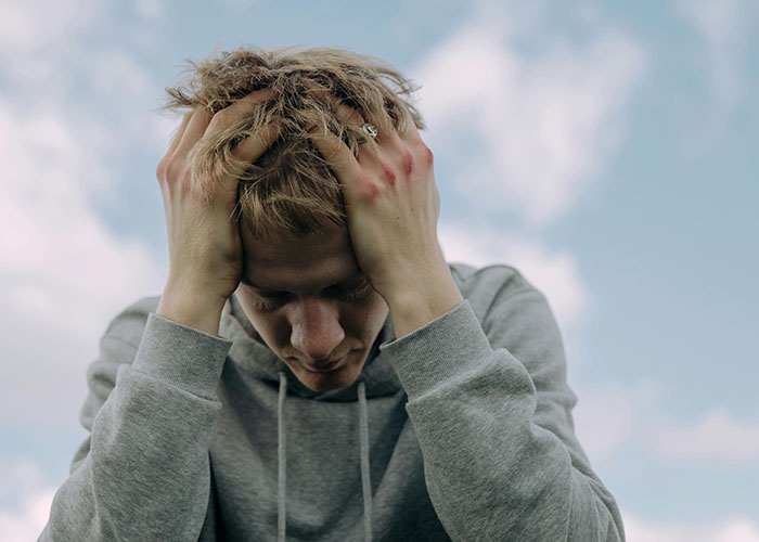 Young man in a gray hoodie holding his head in distress outdoors, illustrating worst cheating stories and emotional pain.