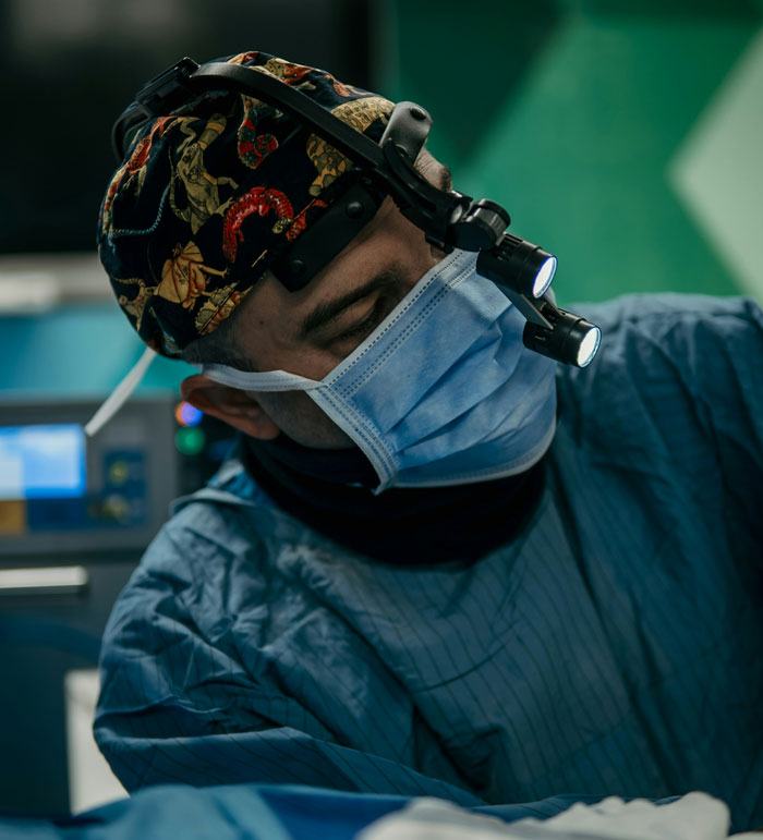 Cirujano en hospital usando mascarilla y lámpara frontal durante procedimiento, simbolizando errores hospitalarios graves.