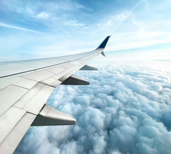 View from airplane window showing wing and clouds, symbolizing travel to a wedding event with unexpected regrets and complications. - 12