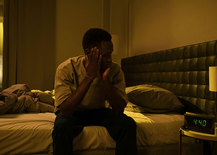 Man sitting on edge of bed at night, looking distressed and deep in thought, illustrating worst cheating stories.
