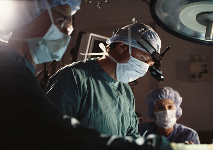 Surgeons wearing masks and scrubs performing surgery under an operating room light in a hospital setting.