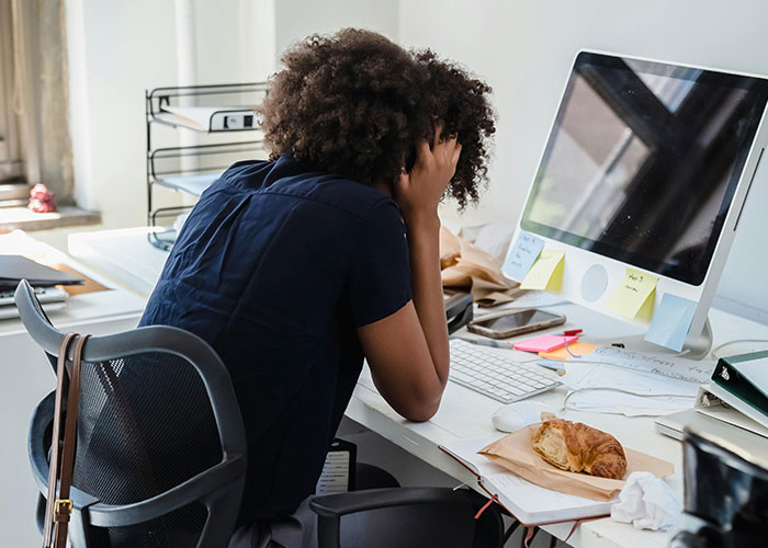Stressed employee at cluttered desk showing signs of micromanagement in a tense workplace environment.