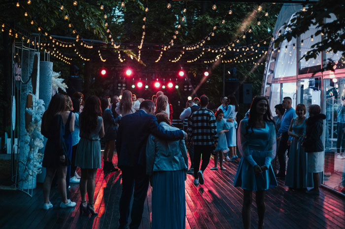 Guests socializing under string lights at a wedding reception, capturing moments people sometimes regret accepting invitations. - 19