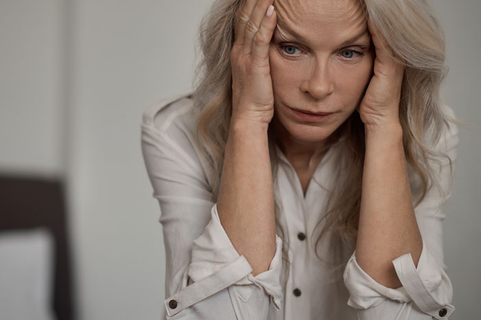 Woman looking contemplative and stressed, holding her head with hands, reflecting on finding herself during a solo trip.