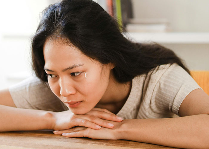 Young woman with tears on her face, resting head on hands, showing emotional distress related to cheating stories.