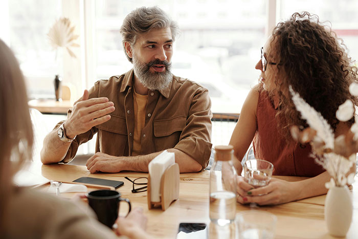 Group of people having a conversation at a table, illustrating holding doors open for big burly men concept.