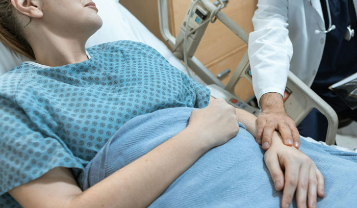 Paciente acostada en hospital mientras un médico sostiene su mano mostrando errores terribles en hospitales.