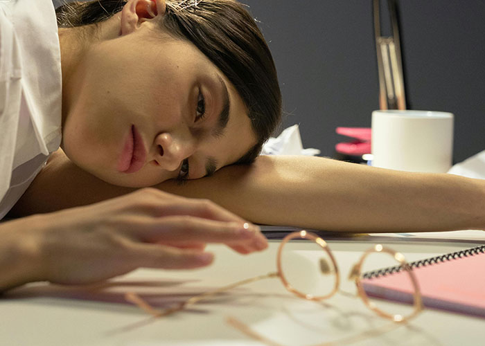 A tired woman resting her head on a desk, showing signs of frustration and stress from micromanagement at work.