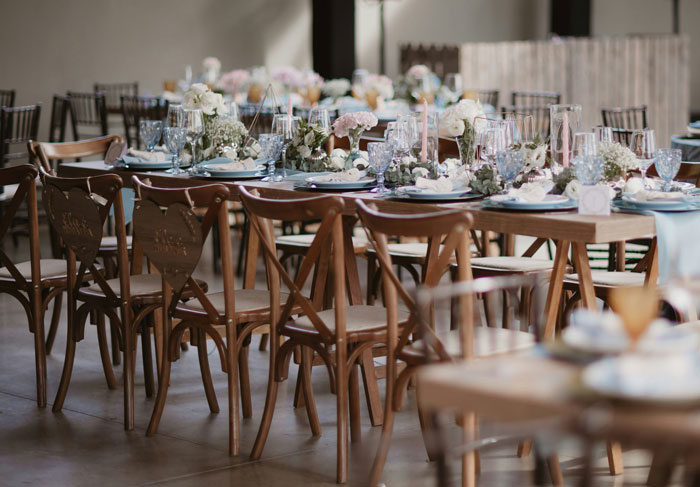 Elegant wedding reception table with wooden chairs, floral centerpieces, and glassware set for guests at a wedding invitation event. - 33