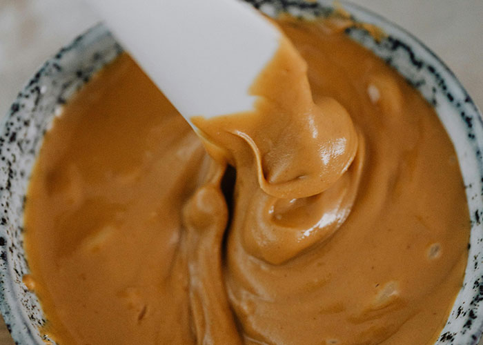 Close-up of a spatula mixing thick peanut butter in a ceramic bowl, illustrating bizarre family food habits.