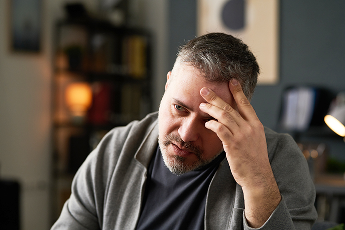 Stressed man sitting indoors, holding his forehead, representing a dad dealing with custody issues during divorce.