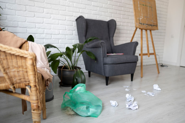 Messy modern living room with oldschool home trends showing scattered papers, a green plastic bag, and mixed furniture styles.