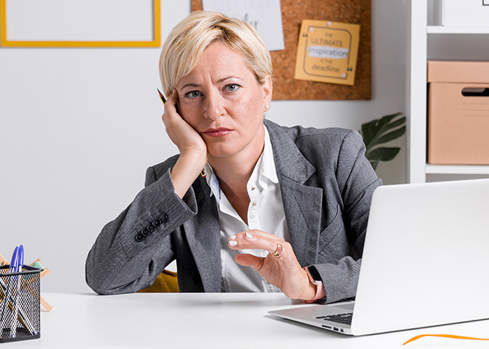 Woman manager looking frustrated while sitting at desk with laptop, dealing with ridiculous complaints from employees.